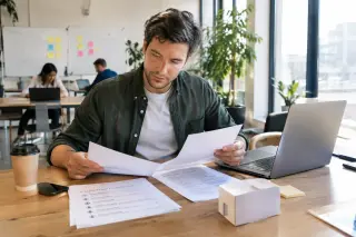 Young entrepreneur in a bright coworking space reviewing customer feedback and prototype on a desk, with a laptop, coffee and interview notes, conveying the early validation phase of a business project.